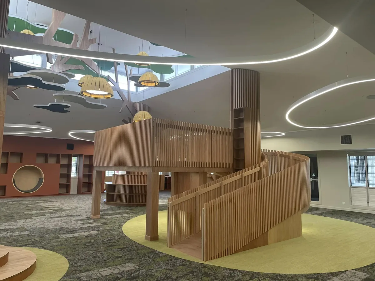School library with a sculptural timber tree column, curved slatted mezzanine and pendant lighting overhead