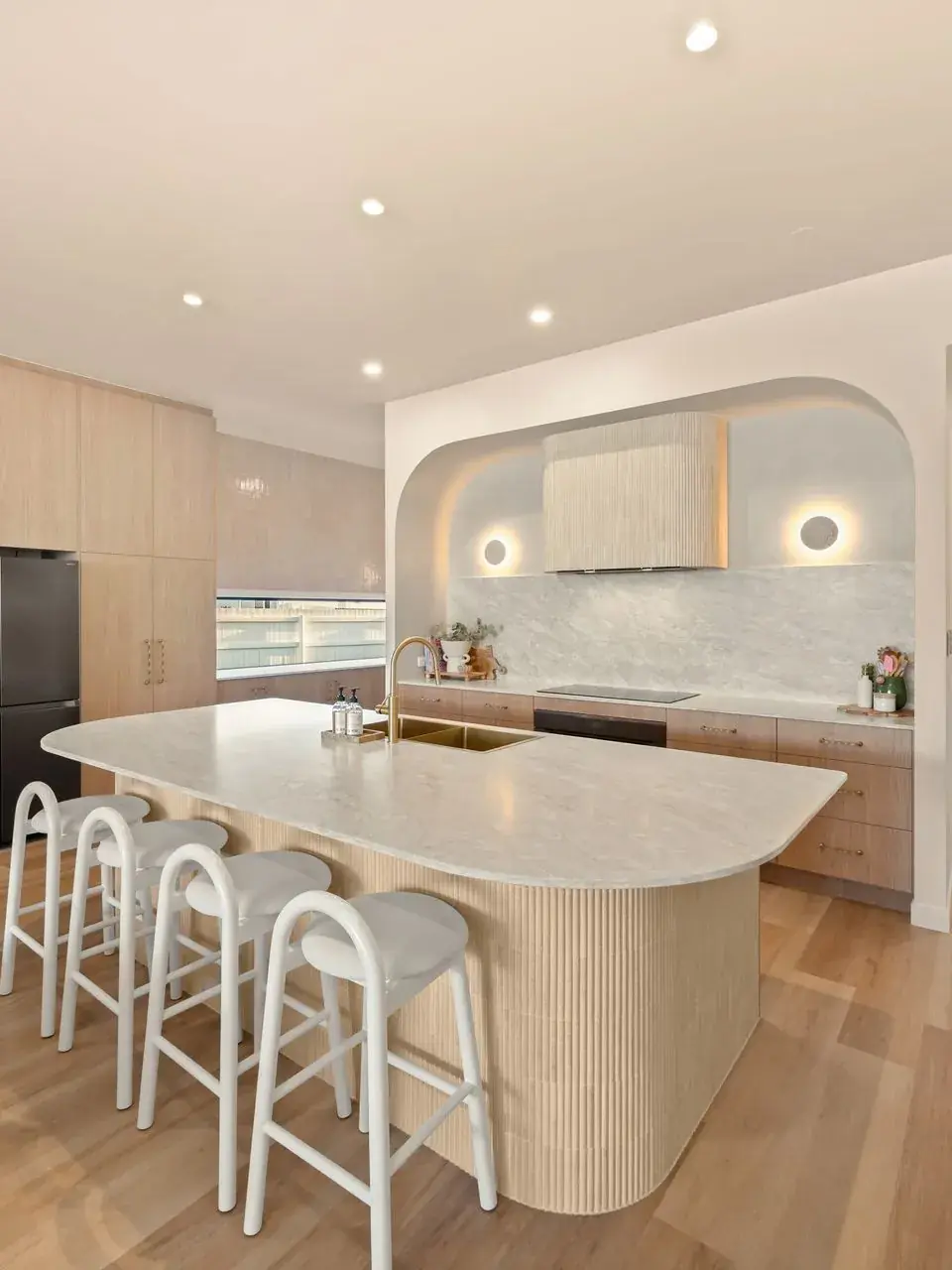 Kitchen with a curved stone island, arched joinery recess and timber cabinetry