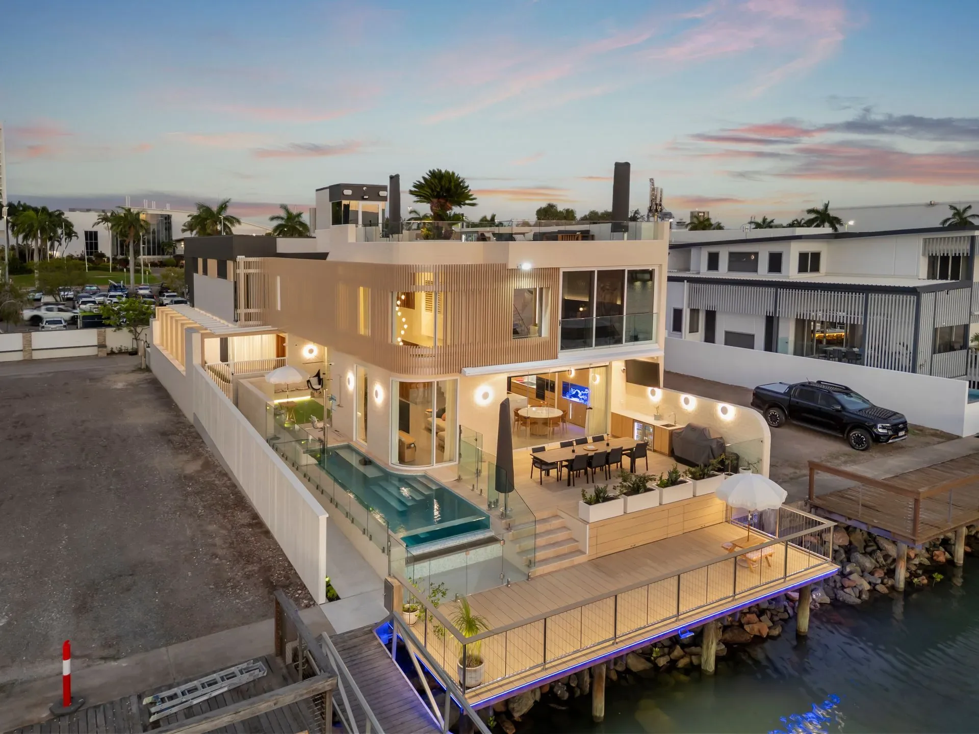 Waterfront residence at dusk seen in full frontage from the water, pool terrace lit
