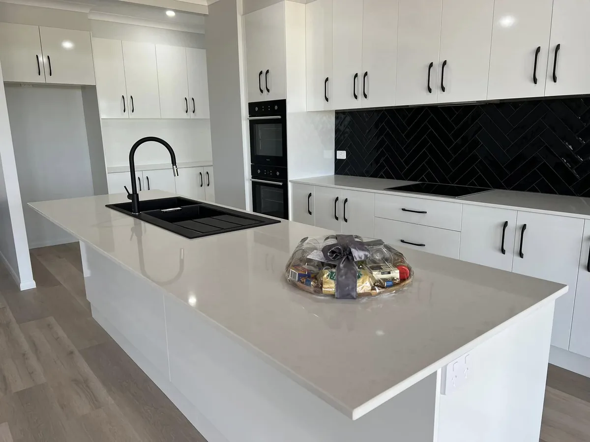 Finished kitchen with a stone island bench, dark splashback and integrated appliances