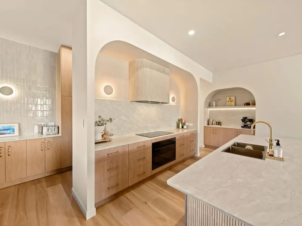 Sculptural kitchen island with softened edges beside an arched joinery recess